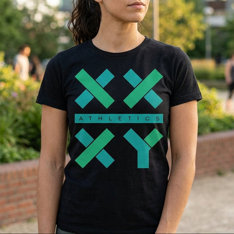 A woman wearing a black short-sleeve t-shirt with a green and teal geometric 'ATHLETICS' graphic, standing in an outdoor park setting.