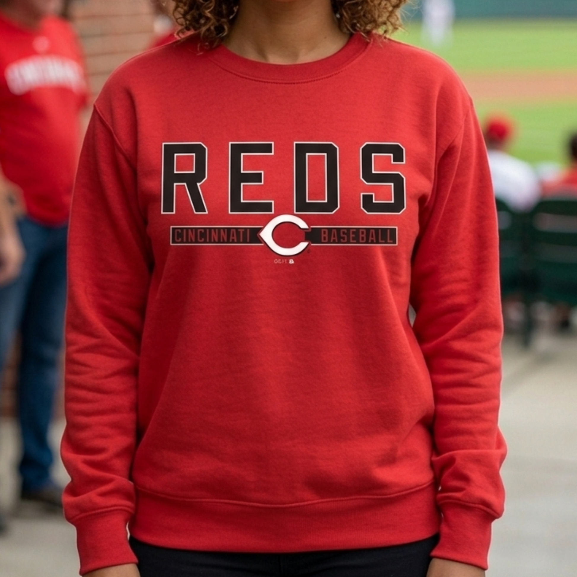 Woman wearing a red 'REDS' sweatshirt at a baseball game